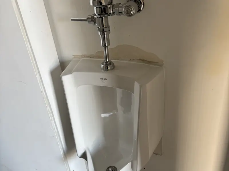 Wall-hung urinal with chrome flush valve in a commercial restroom