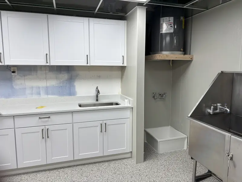 Finished commercial wash room with white cabinets, sink, and stainless steel tub