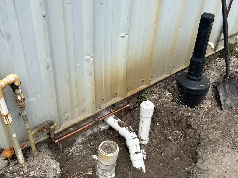 New PVC drain and vent rough-in in the ground beside a building wall