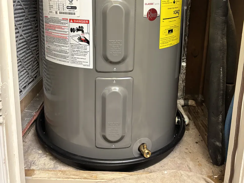 New Rheem electric tank water heater in a closet, set in a new black drain pan